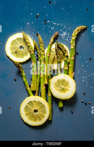 Spargel Kochen mit Zitrone, Salz, Pfeffer schwarz auf blauem Hintergrund Stockfoto