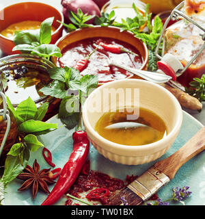 Vorbereitung ein würziges Öl Marinade für ein BBQ mit einer Schüssel mit Olivenöl, Peperoni, frisches Basilikum ad Kräuter und Gewürze in der Nähe zu hohen Winkel anzeigen Stockfoto