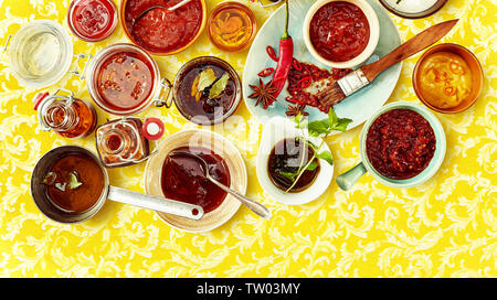 Ansicht von oben der roten Chutney und Salsa mit anderen roten Würzmittel in Schalen über gelb gemusterten Hintergrund. Stockfoto