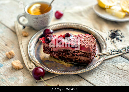 Ein Stück Schokolade Kuchen mit Chocolate Chips und Beeren. Tee mit Zitrone auf dem Tisch Stockfoto