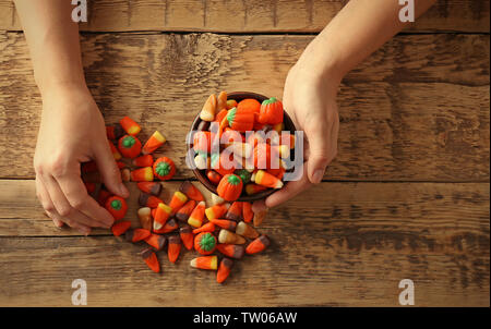 Weibliche Hände halten Schüssel mit Halloween Süßigkeiten auf hölzernen Hintergrund Stockfoto