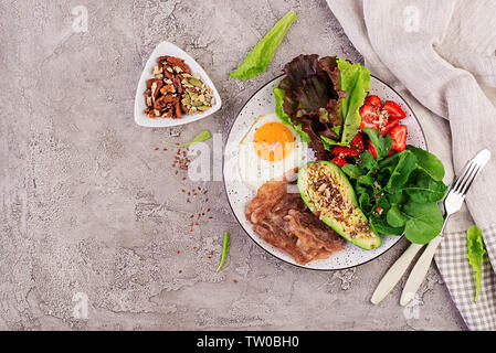 Die Platte mit einer Keto Diät essen. Spiegelei, Speck, Avocado, Rucola und Erdbeeren. Keto Frühstück. Ansicht von oben Stockfoto