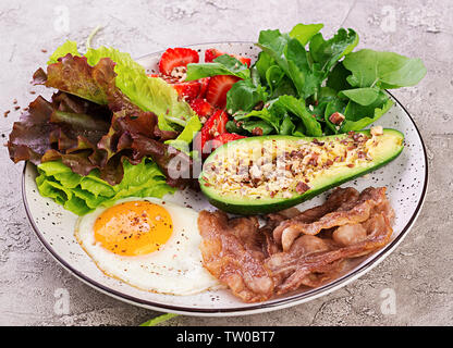 Die Platte mit einer Keto Diät essen. Spiegelei, Speck, Avocado, Rucola und Erdbeeren. Keto Frühstück. Stockfoto