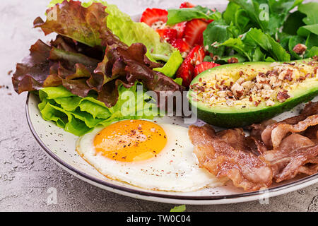 Die Platte mit einer Keto Diät essen. Spiegelei, Speck, Avocado, Rucola und Erdbeeren. Keto Frühstück. Stockfoto