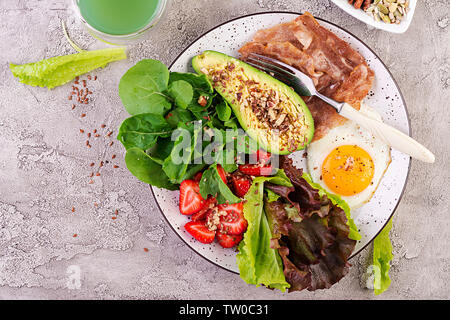 Die Platte mit einer Keto Diät essen. Spiegelei, Speck, Avocado, Rucola und Erdbeeren. Keto Frühstück. Ansicht von oben Stockfoto