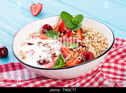 Gesundes Frühstück - Müsli, Erdbeeren, Kirschen, Muttern und Joghurt in eine Schüssel auf einen hölzernen Tisch. Vegetarische Konzept essen. Stockfoto