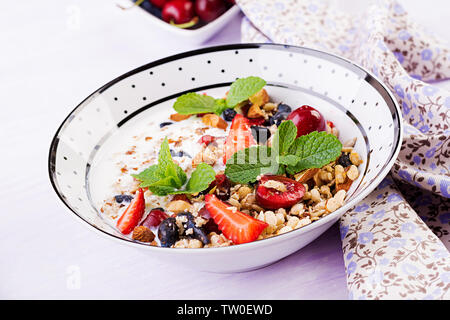 Gesundes Frühstück - Müsli, Erdbeeren, Kirschen, geißblatt Beeren, Nüsse und Joghurt in eine Schüssel geben. Vegetarische Konzept essen. Stockfoto