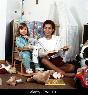 Homestory der deutschen Schlager - Disco- und Popsängerin Ramona Wulf mit Tochter im Kinderzimmer beim Vorlesen, Deutschland Berlin ca. 1985. Homestory der Deutschen Pop, Disco und Pop Sängerin Ramona Wulf mit ihrer Tochter Vorlesen im Kinderzimmer, Deutschland Berlin ca. 1985. Stockfoto