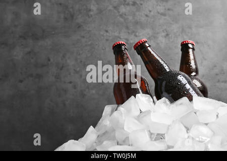 Flaschen Bier in Eis auf grauem Hintergrund Stockfoto