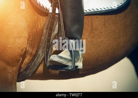 Das Bein des Reiters, der an einer Bucht Pferd sitzt, in einem schwarzen Vintage dirty Boot ruht auf den Steigbügel und wird durch helles Sonnenlicht beleuchtet. Stockfoto