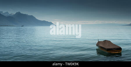 Eine wunderschöne Aussicht auf den Genfer See und die umliegenden Berge im Sommer mit einem einzigen Boot im Vordergrund. Stockfoto