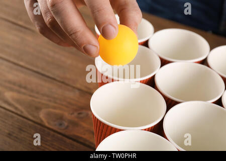 Gelbe Kugel in männlicher Hand und Pappbecher für das Spielen Bier pong angeordnet Stockfoto