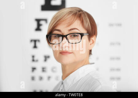 Reife Frau mit Brille mit unscharfen Auge Diagramm auf Hintergrund Stockfoto