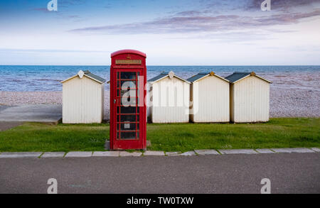 Rote Telefonzelle und Umkleidekabinen am Strand durch das Meer bei Budleigh Salterton, Devon, Großbritannien Stockfoto