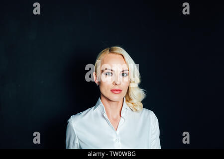 Studio Portrait einer attraktiven Blondine business Frau in einem weißen Hemd und schwarzen Hosen gegen einfachen Hintergrund Stockfoto