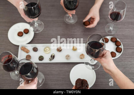 Weibliche Hände halten Gläser Rotwein und Süßigkeiten über Holz- Tabelle Stockfoto