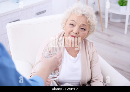 Ältere Frau unter Glas Wasser in hellen Zimmer Stockfoto