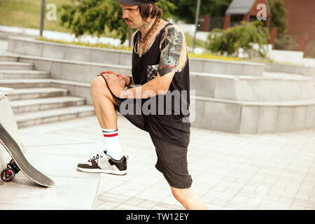 Skateboarder Vorbereitung für das Reiten an der Hauptstraße der Stadt in cloudly Tag. Junger Mann in Sneakers und Kappe mit einem Longboard auf dem Asphalt. Konzept der Freizeitgestaltung, Sport, Extreme, Hobby und Bewegung. Stockfoto