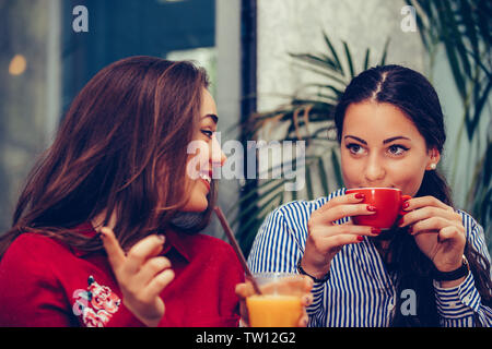 Bild eines zwei glückliche Mädchen Freunden im Cafe sitzen Sprachen miteinander Kaffee trinken, Pointing Finger zu empfehlen. Stockfoto