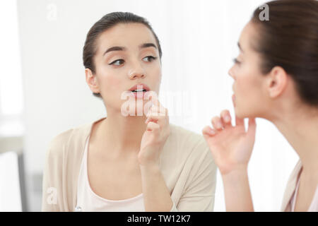 Schöne Frau Anwendung Creme auf die Lippen in der Nähe von Spiegel Stockfoto