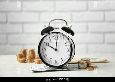 Wecker und Geld auf weißen Tisch gegen die Wand Hintergrund Stockfoto