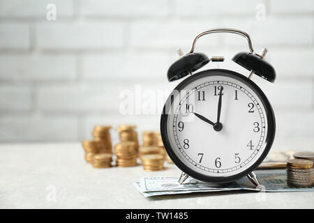 Wecker und Geld auf weißen Tisch gegen die Wand Hintergrund Stockfoto