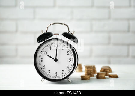 Wecker und Münzen am weißen Tisch gegen die Wand Hintergrund Stockfoto