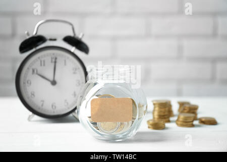 Glas mit Münzen und Wecker gefüllt auf Hintergrund Stockfoto