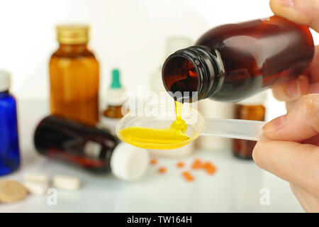 Hände gießen Hustensaft in Löffel auf unscharfen Hintergrund von Arzneimitteln Stockfoto