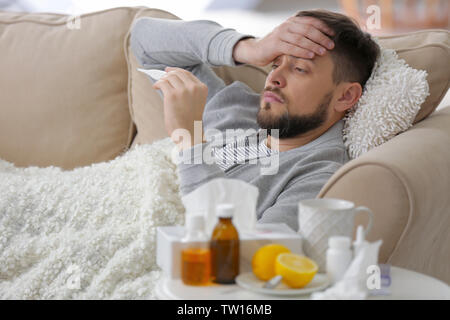 Junge kranke Mann mit elektronische Thermometer liegend auf dem Sofa zu Hause Stockfoto