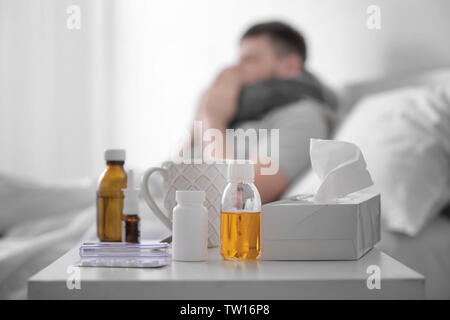 Medikamente und heiße Tasse Tee mit unscharfen kranker Mann im Hintergrund Stockfoto