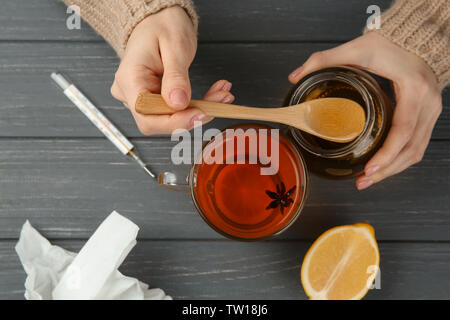 Frau Hände Honig in einer Tasse Tee auf hölzernen Hintergrund Stockfoto