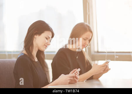 Mitarbeiter können Sie über Ihr Smartphone an einem Tisch in einem Cafe sitzen. Mensch und Technik Stockfoto