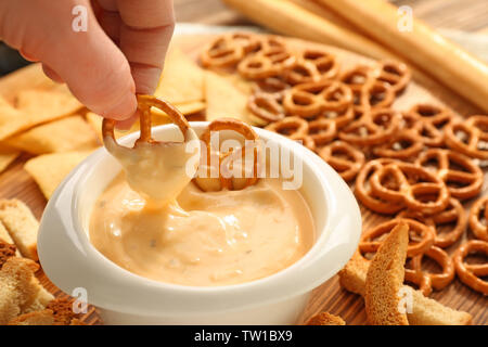 Weibliche Hand tauchen Brezel in der Schüssel mit Bier Käse dip, Nahaufnahme Stockfoto