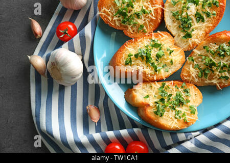 Leckere Brotscheiben mit geriebenem Käse, Knoblauch und Kräutern auf Platte Stockfoto