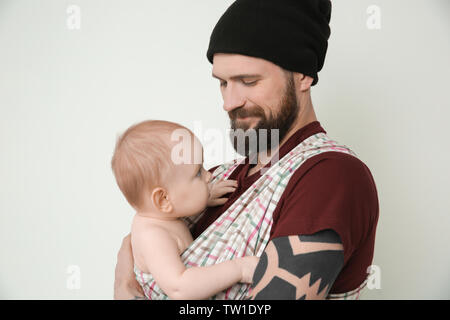 Stattliche tätowierten jungen Mann mit niedlichen kleinen Baby auf hellen Hintergrund Stockfoto