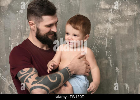 Stattliche tätowierten jungen Mann mit niedlichen kleinen Jungen auf grauem Hintergrund Stockfoto