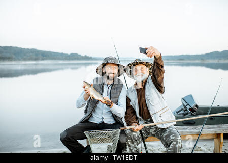 Großvater mit Sohn Spaß, wodurch selfie Foto zusammen mit fangfrischem Fisch auf dem See in den frühen Morgenstunden Stockfoto