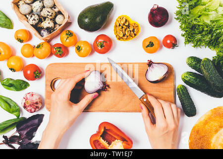 Ansicht von oben weibliche Hände vorbereiten gesunder Salat auf Holz Schneidebrett neben frischem Gemüse, Nüsse und grünen Salat, flach Zusammensetzung auf Weiß Stockfoto