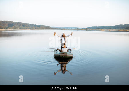 Glückliche Menschen, die frisch gefangenen Fische beim Stehen auf dem Boot mit Großvater auf den See in den frühen Morgenstunden Stockfoto