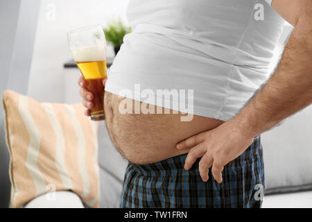 Mann mit großen Bauch holding Glas Bier zu Hause Stockfoto