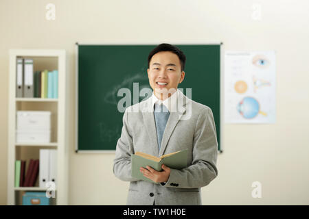 Schönen asiatischen Lehrer mit Buch im Klassenzimmer Stockfoto