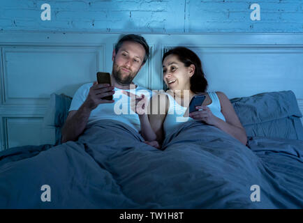 Lächelnd attraktive junge Männer und Frau Paar mit Smartphone auf dem Bett zusammen liegen. Gerne Freund und Freundin Kontrolle soziale Netzwerke oder mobil Stockfoto