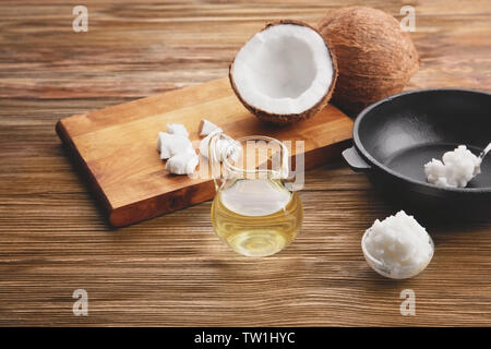 Glaskanne mit Kokosöl und Küchenutensilien auf hölzernen Hintergrund Stockfoto