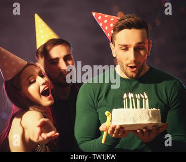 Hübscher junger Mann bläst die Kerzen auf der Geburtstagstorte bei Party Stockfoto