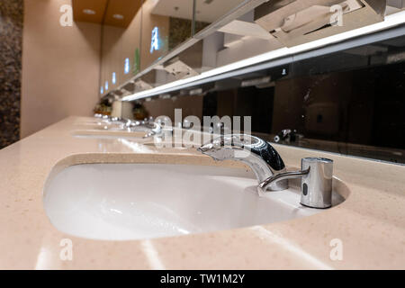 Armaturen mit Waschbecken in öffentlichen Toiletten, aus der Nähe. Modernes Waschbecken mit Spiegel in öffentlichen Wc Stockfoto