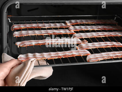 Weibliche hand Kontrolle Streifen Speck auf Grill im Ofen Stockfoto