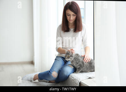 Schöne junge Frau mit niedlichen Katze sitzt auf der Fensterbank zu Hause Stockfoto