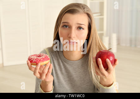 Schöne junge Frau, die Wahl zwischen Apple und Donut Stockfoto