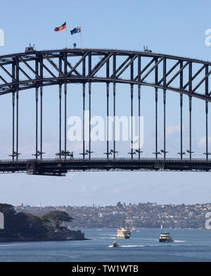 Detail der Sydney Harbour Bridge mit National Flagge Aborigines Flagge. Gärten von Admiralty House befinden sich unten links. Boote in Betrieb sind Stockfoto